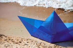 barco de papel azul de origami en la playa de arena para el diseño conceptual, hermoso barco de papel en la costa, primer plano foto