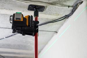 Laser level measuring tool with visible green laser beam on wall for installing stretch ceiling photo