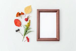 Autumn floral composition. Vertical frame mockup chokeberry rowan berries colorful leaves dogrose flowers on white background. Fall natural plants ecology concept. Flat lay top view, copy space photo