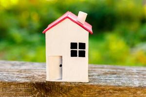 casa modelo de juguete blanco en miniatura con fondo de madera cerca de fondo verde. aldea ecológica, fondo ambiental abstracto. concepto de ecología de casa de ensueño de seguro de propiedad de hipoteca de bienes raíces. foto