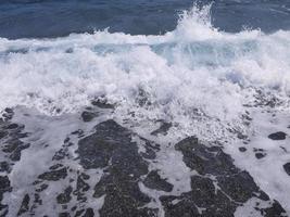 mar azul profundo en la playa negra con una ola de salpicaduras blancas para papel tapiz de fondo foto