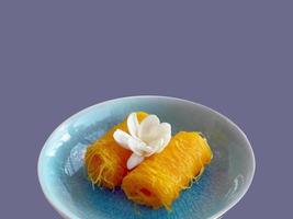 Close up of Thai style Fios de ovos, rolled golden egg yolk thread, traditional sweet food dessert in blue celadon plate, cut out isolated, copy space with clipping path photo