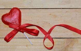 Chocolate heart wrapped in red and Red Ribbon on wood. valentine concept. Space for text. photo