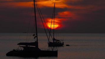 silhouet van een jacht op de achtergrond van een rode zonsondergang aan de oceaankust. ontspannend uitzicht op de zonsondergang video