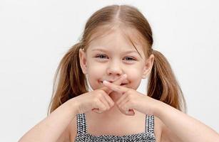 Child holding crossed fingers on mouth photo