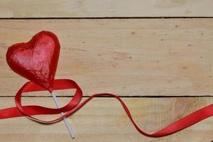 Chocolate heart wrapped in red and Red Ribbon on wood. valentine concept. Space for text. photo