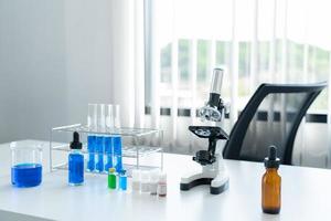 ciencia, herramientas de laboratorio colocadas en la mesa blanca. microscopio, tubos en la rejilla y espécimen líquido azul foto