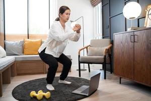 sporty woman in sportswear is sitting on carpet at home in the living room exercising, healthy and lifestyle concept.