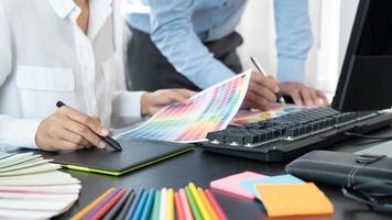 Graphic designer or creative working together coloring using graphics tablet and a stylus at desk with colleague.