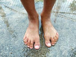 los pies del niño están en un charco en un viejo piso de concreto frente a la casa. después de fuertes lluvias para sentirse divertido foto