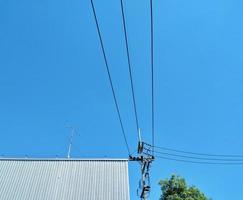 postes eléctricos con cables conectados a la fábrica con cielos azules dan la idea de usar electricidad para la producción. foto