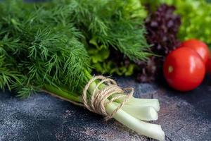 Fresh vegetables for salad. Tomatoes and lettuce, cucumbers with zucchini and cabbage with dill. Spring harvest, benefits and vitamins. On a dark background. photo