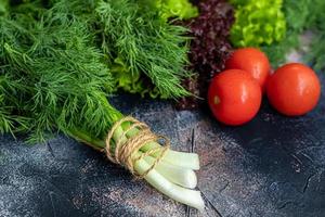 Fresh vegetables for salad. Tomatoes and lettuce, cucumbers with zucchini and cabbage with dill. Spring harvest, benefits and vitamins. On a dark background. photo