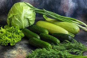 Fresh vegetables for salad. Tomatoes and lettuce, cucumbers with zucchini and cabbage with dill. Spring harvest, benefits and vitamins. On a dark background. photo