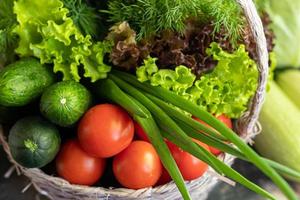 Fresh vegetables for salad in a basket. Tomatoes and cucumbers with zucchini and cabbage with dill. Spring harvest, benefits and vitamins. On a dark background. photo