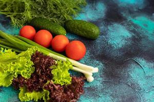Fresh vegetables for salad. Tomatoes and lettuce, cucumbers with zucchini and cabbage with dill. Spring harvest, benefits and vitamins. On a dark background. photo