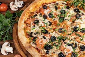 Pizza with bacon and cheese, herbs and cherry tomatoes. With mozzarella, shrimps and octopuses, mussels and other products on a wooden background. photo