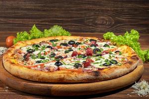 Pizza with bacon and cheese, herbs and cherry tomatoes. With mozzarella, shrimps and octopuses, mussels and other products on a wooden background. photo