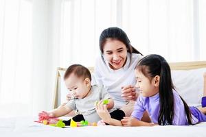 madre ocupada trabajando en la computadora portátil, jugando con el bebé y hablando con la pequeña hija foto