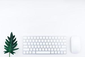 mesa de oficina o escritorio de oficina. hay teclado de computadora blanco, mouse blanco y hoja de monstera verde foto