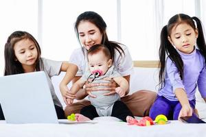 Busy single mom concept, mother working on laptop and caring for her baby and little daughte photo