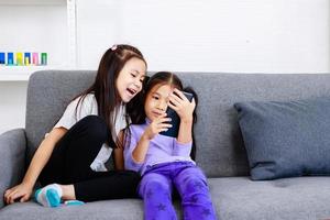 dos niñas felices y lindas que usan un teléfono inteligente para jugar o estudiar juntas en casa foto