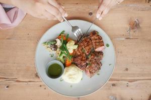 top view of women hand eating beef steaks meat with vegetables on a plate photo