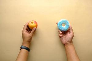 Mano sujetando donas y manzana en mano sobre fondo azul. foto