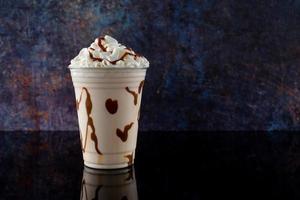 Vanilla milkshake with chocolate syrup in clear glass on dark background. photo