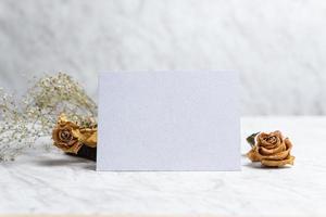 tarjeta en blanco y flores marchitas sobre fondo de mármol