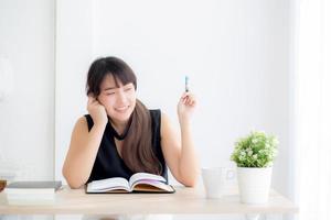Young asian woman writer smiling thinking idea and writing on notebook or diary with happy on desk office, lifestyle of asia girl is success, female planning working, education and business concept. photo