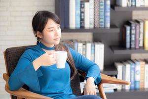 Young asian woman sitting on chair with comfort and relaxing in living room at home drinking a cup of coffee or tea or beverage, lifestyle asia girl leisure healthy and wellness for satisfied. photo