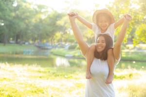 Beautiful young asian mother carrying little daughter with smile, child ride the neck on mom with happiness and cheerful together in the park, lifestyle family with enjoy and fun concept. photo