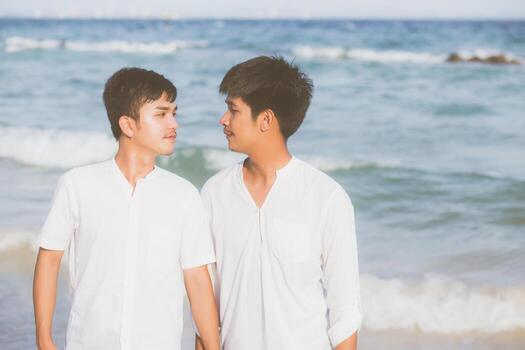Homosexual portrait young asian couple standing together on beach in summer, asia gay holding hands going sea for leisure and relax with romantic and happy in vacation at sea, LGBT with legal concept. photo