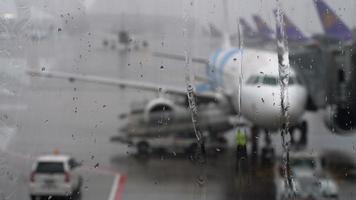 tempesta in aeroporto. vista dell'aereo attraverso gocce di pioggia e ruscelli. temi del tempo e del volo in ritardo o cancellato. video