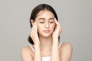 hermosa joven modelo asiática toca su cara con una piel limpia y fresca perfecta sobre fondo gris. cuidado facial, tratamiento facial, cosmetología, cirugía plástica, hermoso retrato de niña en estudio. foto