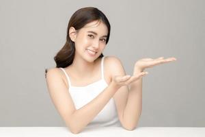 Beautiful young Asian woman model presenting or showing open hand palm with copy space with clean fresh skin on grey background. Face care, Facial treatment, Cosmetology, Plastic Surgery. photo