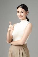 Confident Asian woman showing like thumb up and looks at the camera isolated over grey background. Portrait of pretty girl in studio. photo