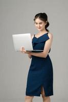 Young energetic Asian business woman holding laptop on gray background. Portrait of pretty girl in studio. Small business SME, freelance online, e-commerce Concept. photo