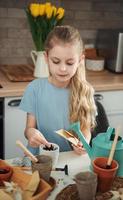 niña sentada en la mesa en casa, sembrando semillas en macetas. foto