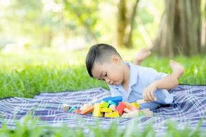 el niño pequeño está jugando por la idea y la inspiración con un bloque de juguete en el campo de hierba, un niño aprendiendo con un bloque de construcción para la educación, actividad infantil y juego en el parque con felicidad en el verano. foto