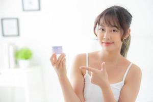 hermoso retrato joven mujer asiática sosteniendo y señalando la presentación de productos de crema o loción, la chica de belleza asiática muestra maquillaje cosmético e hidratación para el cuidado de la piel, el concepto de salud y bienestar. foto