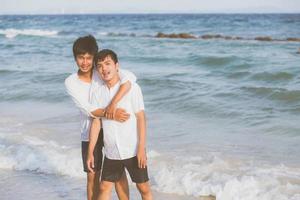 retrato homosexual joven pareja asiática de pie abrazo juntos en la playa en verano, turismo gay de asia para el ocio y relajarse con romanticismo y felicidad en vacaciones en el mar, concepto lgbt. foto