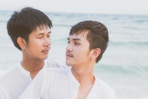 retrato homosexual joven pareja asiática de pie abrazo y miran juntos en la playa en verano, turismo gay de asia para el ocio y relajarse con romántico y feliz en vacaciones en el mar, concepto legal lgbt. foto