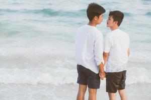 Back view young asian couple standing together on beach in summer, asia gay holding hands going sea for leisure and relax with romantic and happy in vacation at sea, LGBT with legal concept. photo