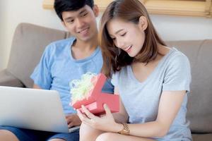 Young asian couple celebrate birthday together, asia man giving gift box present to woman for surprise at living room, female feeling happy and excited anniversary, holiday valentine concept. photo