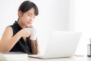 Beautiful young freelance asian woman smiling working and on laptop computer at desk office with professional, girl using notebook and drink coffee, business and lifestyle concept. photo