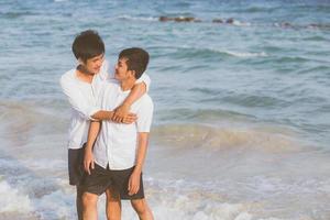 retrato homosexual joven pareja asiática de pie abrazo juntos en la playa en verano, turismo gay de asia para el ocio y relajarse con romanticismo y felicidad en vacaciones en el mar, concepto lgbt. foto