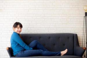 Beautiful portrait young asian woman sitting and smiling happy and looking at camera on sofa with casual at living room, girl cheerful and relax on couch at home, lifestyle concept. photo