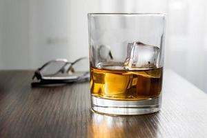 Glass of whiskey, brandy, cognac with ice cubes on wooden table desk with glasses. Mockup of product, gift for man photo